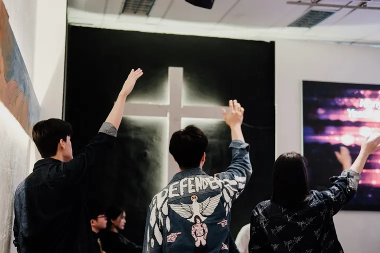 Hands raised in worship before the illuminated cross
